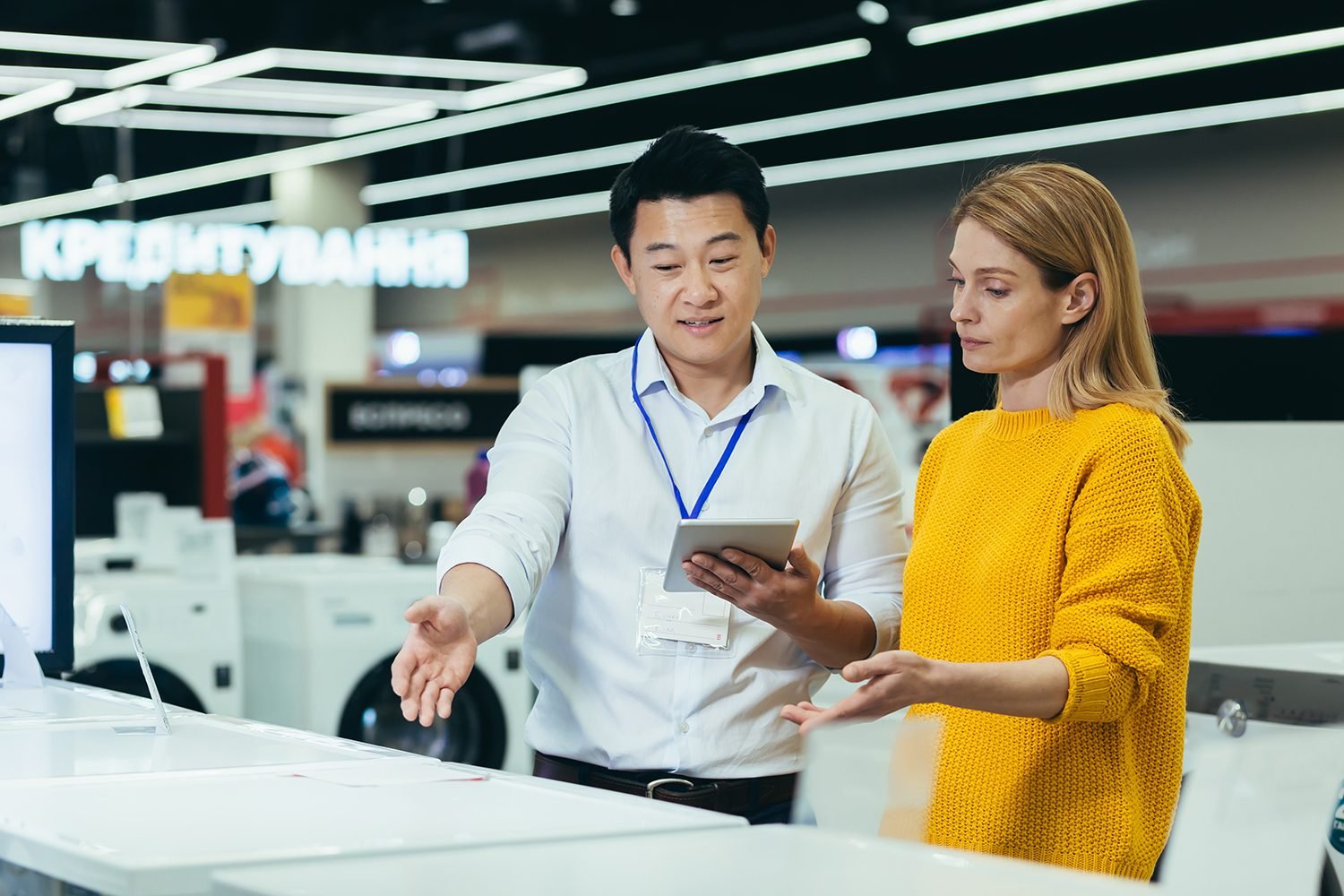 Asian consultant salesman in electronics and household appliances store, selling a working machine to a woman, recommending and approving the choice